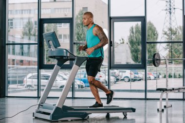 spor salonunda koşu bandı üzerinde çalışan genç Afro-Amerikan sporcu yan görünüm