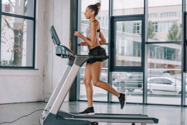 Afro-Amerikan sporcumuz spor salonunda koşu bandı üzerinde çalışan yan görünüm