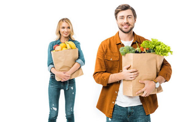 happy young man holding shopping bag with products while his girlfriend standing behind isolated on white