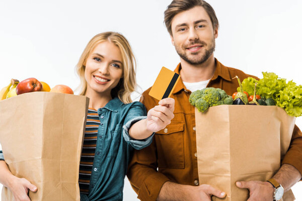 happy girl showing credit card while her boyfriend standing near with shopping bags full of products isolated on white