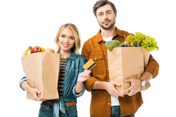 portrait of young woman showing credit card while her boyfriend standing near with shopping bags full of products isolated on white