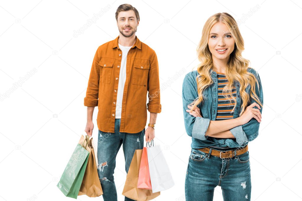 beautiful smiling woman posing with crossed arms while her boyfriend standing behind with shopping bags isolated on white