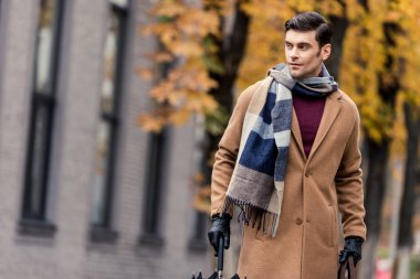 handsome stylish man in coat with umbrella walking by autumnal street clipart