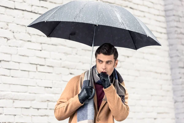 stock image stylish man in coat and scarf with umbrella standing in front of brick wall on street