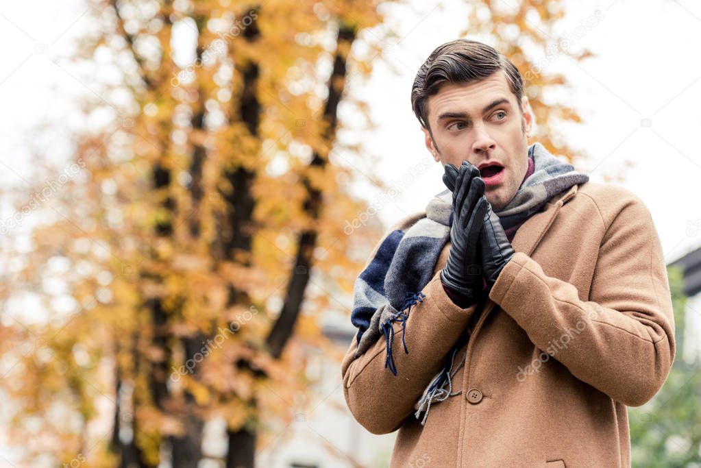 bottom view of attractive stylish man in coat freezing on autumnal street