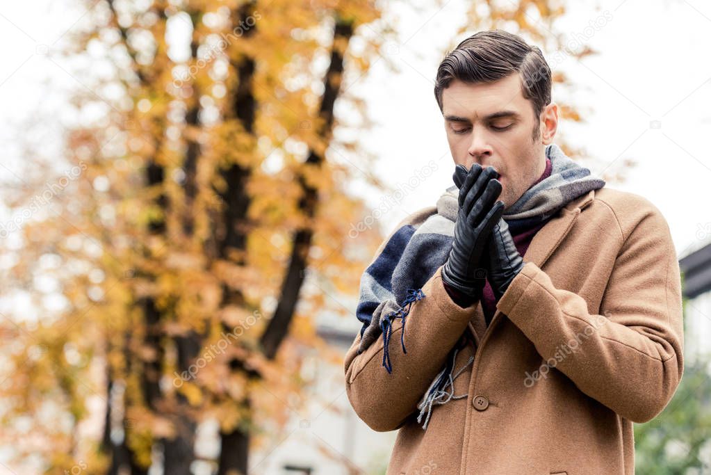 bottom view of stylish man in coat freezing on autumnal street