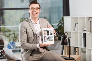 İşyerinde masasında oturan ve ekranda tablet pinterest Web sitesi ile tutarak yakışıklı mutlu işadamı