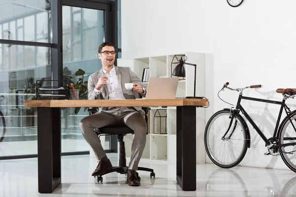英俊快乐的商人与一杯咖啡坐在工作场所在现代办公室 — 免费的图库照片