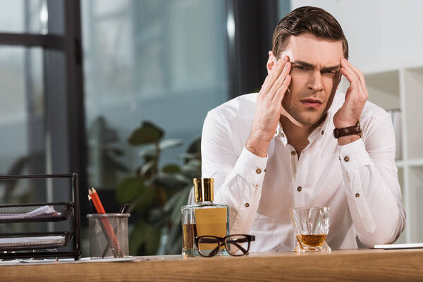 подавленный бизнесмен со стаканом виски, страдающий от головной боли в офисе
