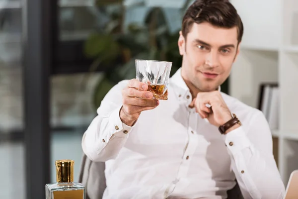 Przystojny Biznesmen Trzymając Szklankę Whisky Patrząc Kamery Biurze — Zdjęcie stockowe