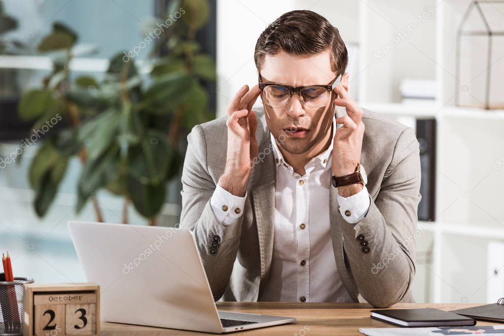 overworked businessman suffering from headache while sitting at workplace in office