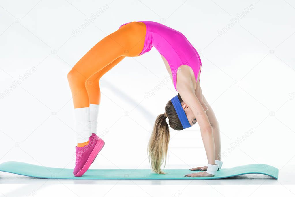 side view of athletic young woman doing bridge exercise on yoga mat on grey