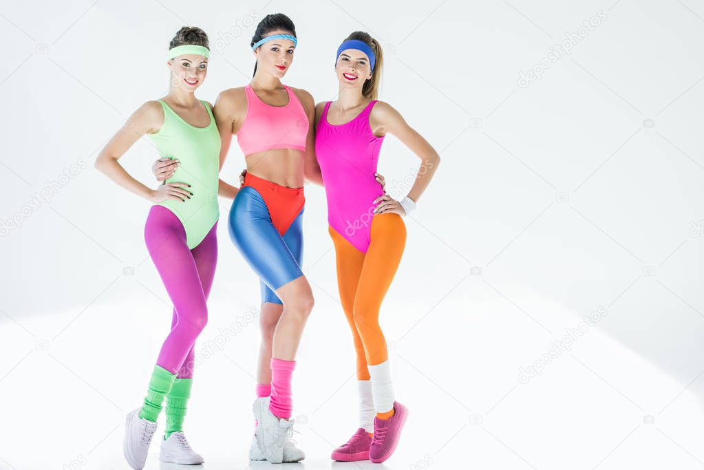 attractive young women in 80s style sportswear standing together and smiling at camera on grey