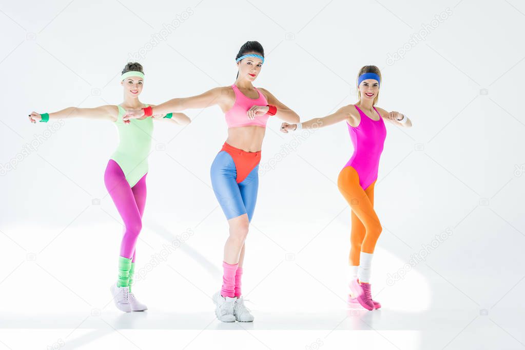 athletic young women exercising together and looking at camera on grey