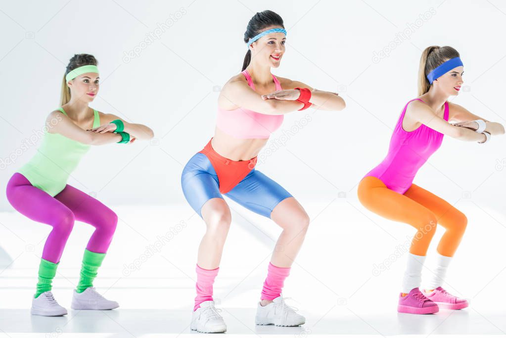 full length view of sporty smiling girls doing squat on grey