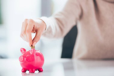 close-up partial view of woman putting coin into pink piggy bank   clipart