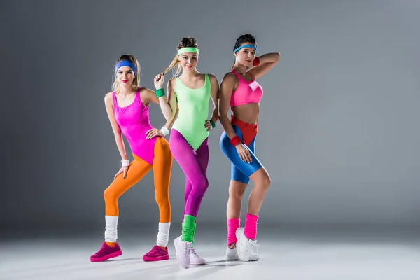 attractive sporty girls in 80s style sportswear posing together and looking at camera on grey