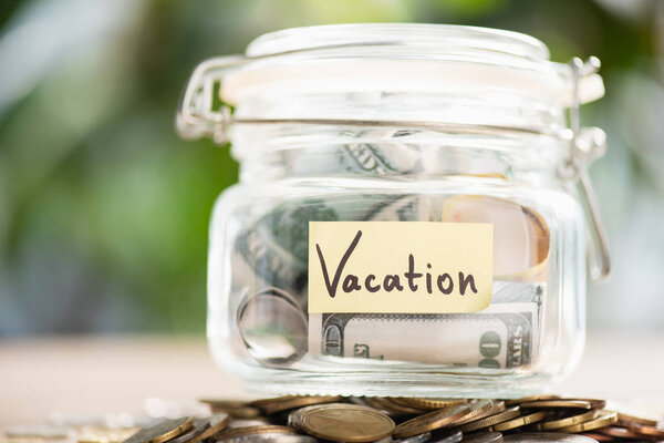 close-up view of glass jar with dollar banknotes and inscription vacation