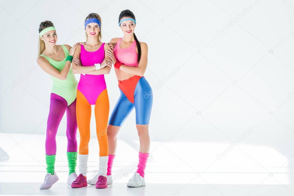 beautiful sporty young women in 80s style sportswear smiling at camera on grey