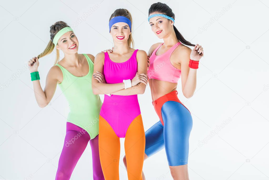 beautiful athletic girls in 80s style sportswear smiling at camera isolated on grey