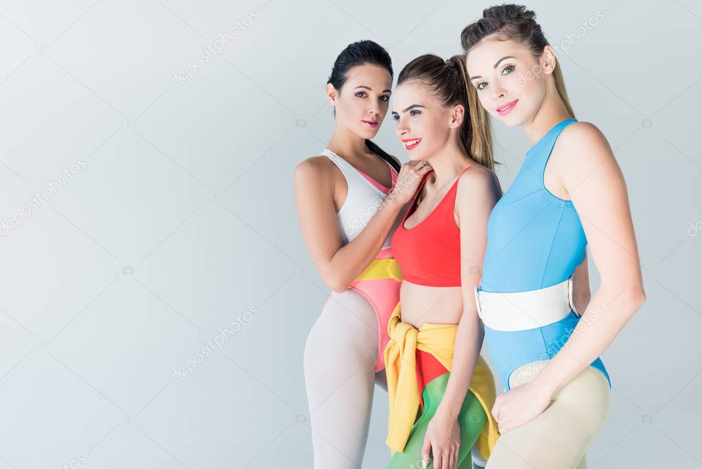 beautiful sporty girls in bodysuits standing together isolated on grey