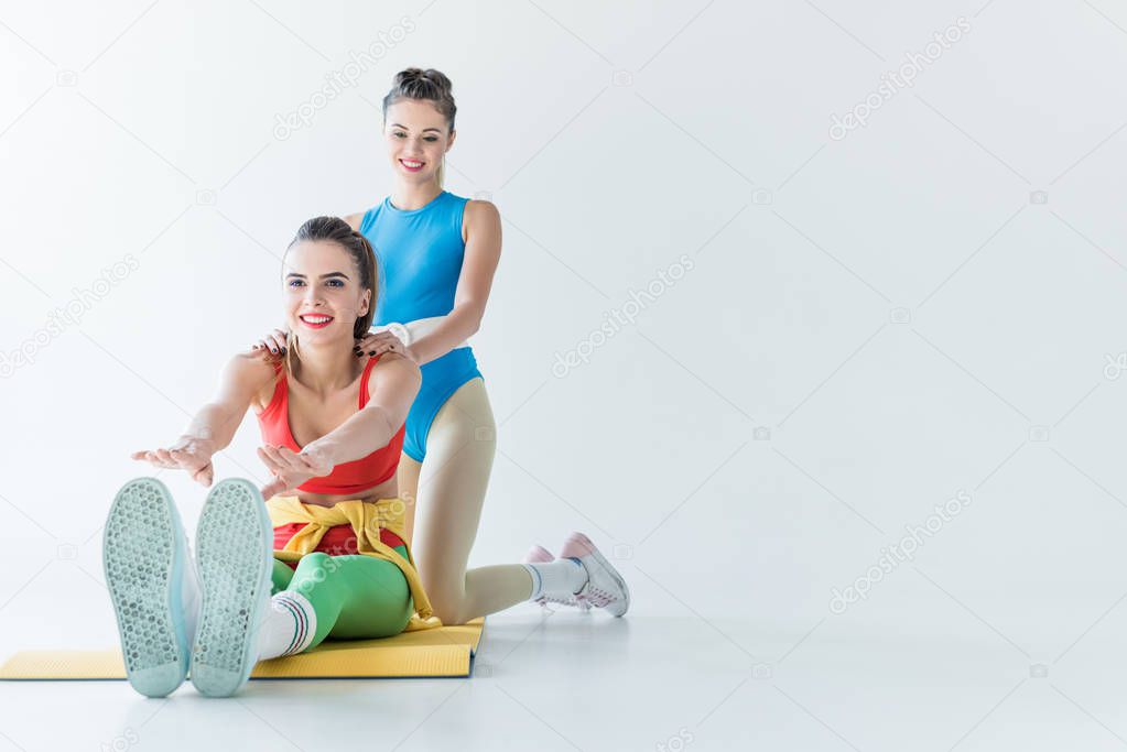 smiling sporty girls stretching and training together on grey