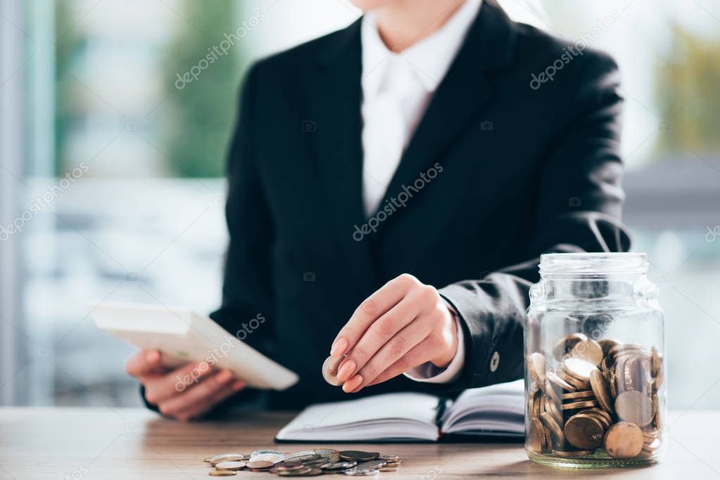 cropped shot of businesswoman working and putting coin on pile