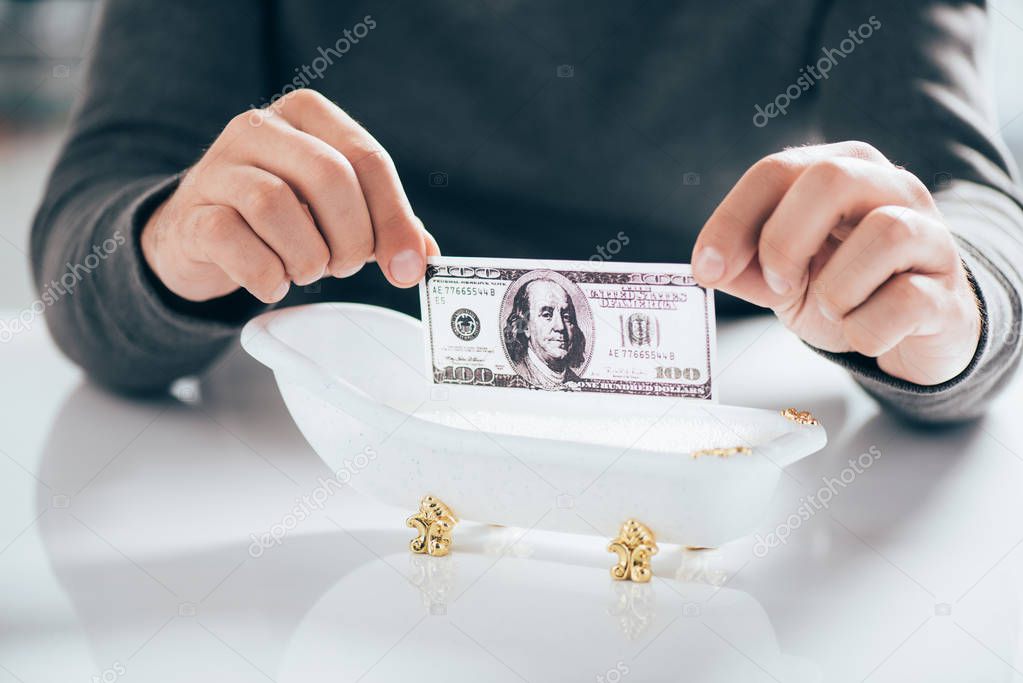 cropped shot of man holding dollar banknote above tub, money laundering concept