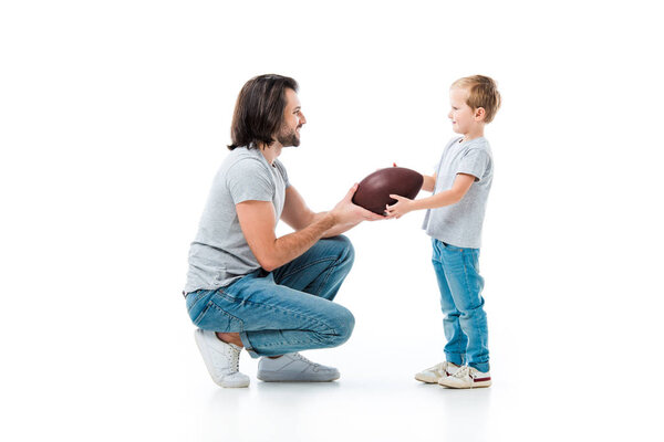 Caring father giving american football ball to his son isolated on white