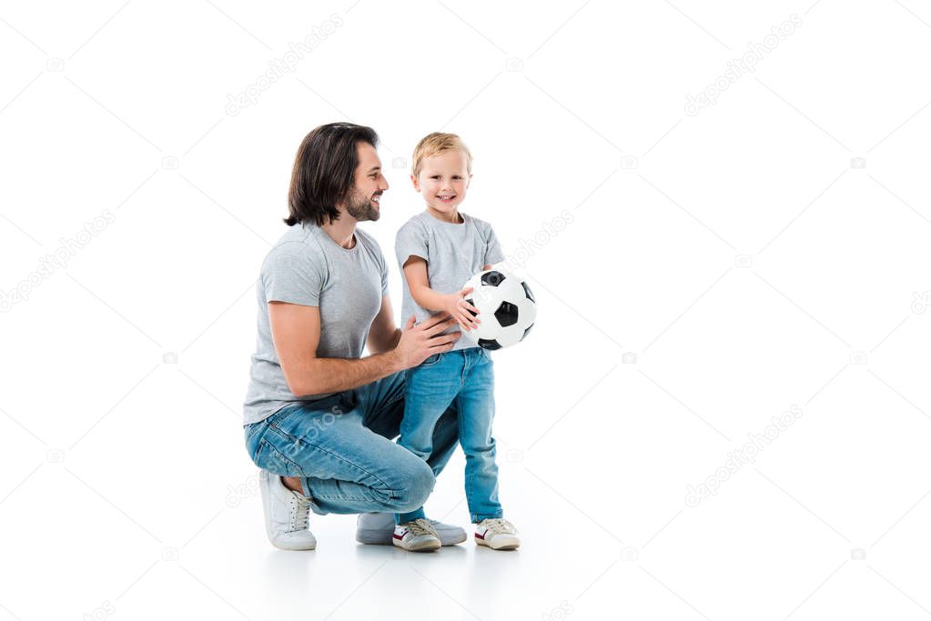 Father hugging and looking at his happy son with soccer ball isolated on white