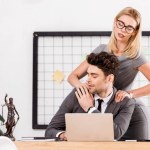 Geschäftsfrau massiert Kollegin am Arbeitsplatz im Büro, Konzept für Büroromantik