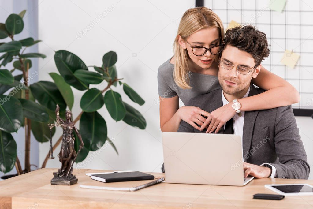 portrait of female lawyer hugging colleague at workplace with laptop in office, flirt and office romance concept