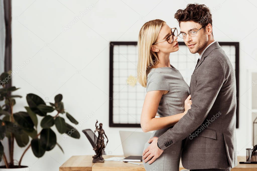 young lawyers hugging each other while standing in office, flirt and office romance concept