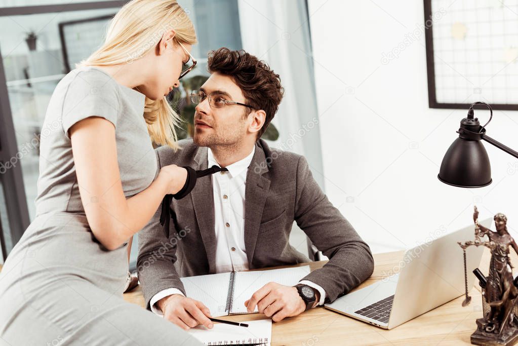 businesswoman holding colleagues tie while flirting at workplace in office