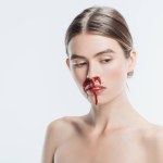Голая женщина с кровью и травмой на лице изолированы на белом