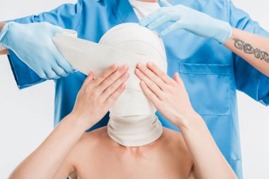 close up of plastic surgeon in gloves taping up woman face with bandage isolated on white clipart