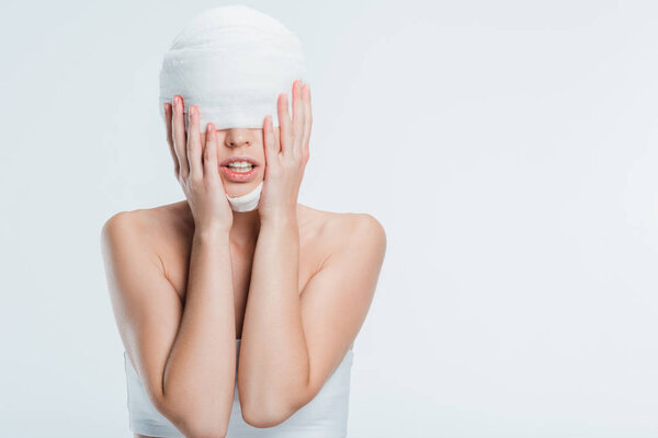 woman with bandages touching head after plastic surgery isolated on white