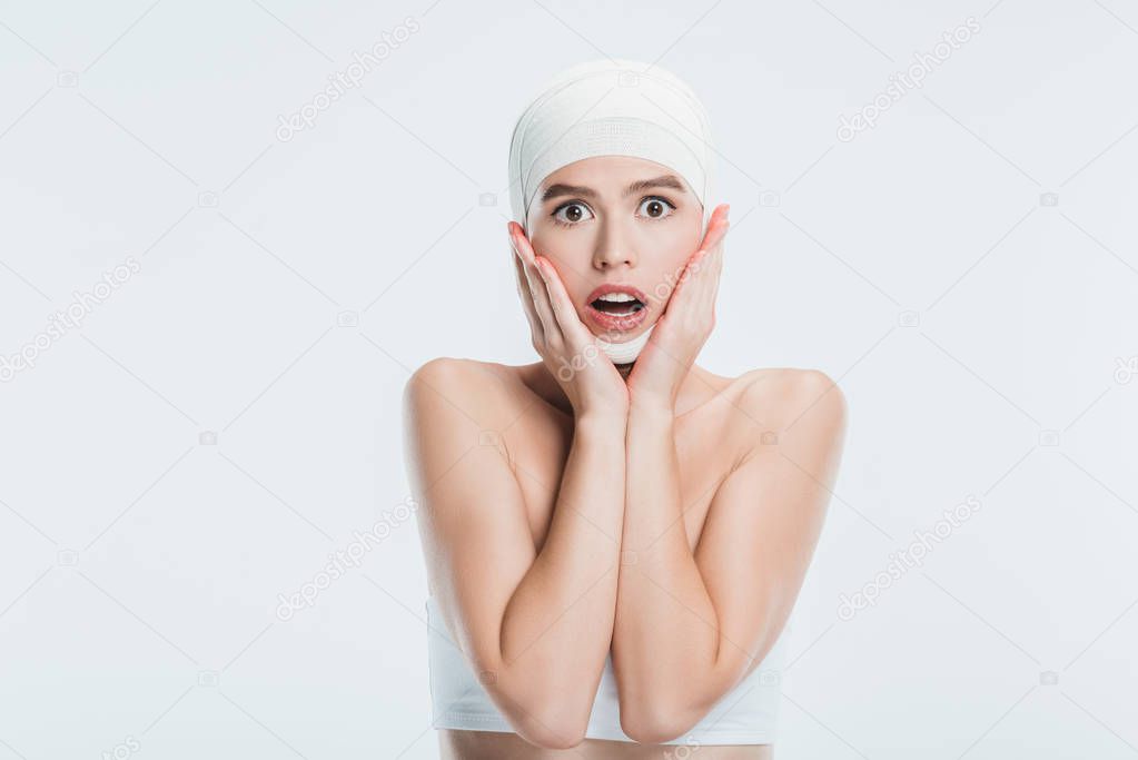 scared woman with bandages over head after plastic surgery isolated on white