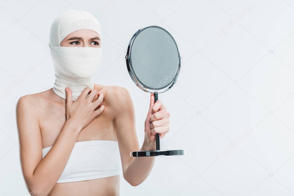 frightened woman after plastic surgery on face looking at mirror isolated on white