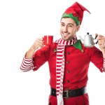 Happy man in christmas elf costume holding red cup and metal kettle isolated on white