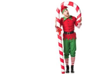 şaşırmış adam Noel elf kostüm üzerine beyaz izole büyük şeker kamışı altında duran
