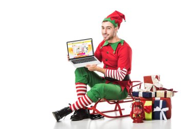 adam kızak üzerinde oturan ve üzerinde beyaz izole ekran dizüstü aliexpress Web sitesi ile tutarak Noel elf kostümü