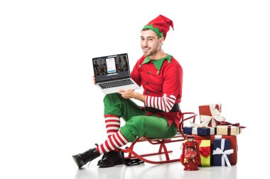 adam kızak üzerinde oturan ve üzerinde beyaz izole ekran dizüstü LinkedIn Web sitesi ile tutarak Noel elf kostümü