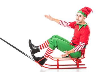 excited happy man in christmas elf costume riding sleigh and looking at camera isolated on white clipart