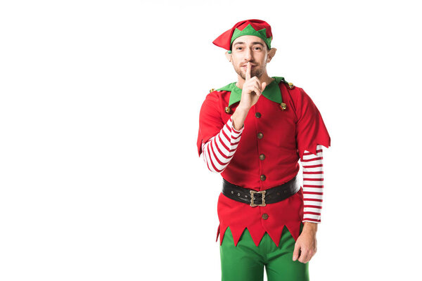 мужчина в рождественском костюме эльфа показывает знак молчания и смотрит на камеру, изолированную на белом

