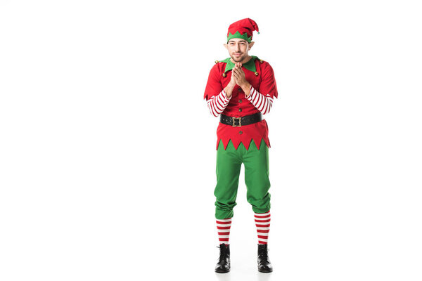 excited man in christmas elf costume looking at camera and rubbing hands in anticipation isolated on white