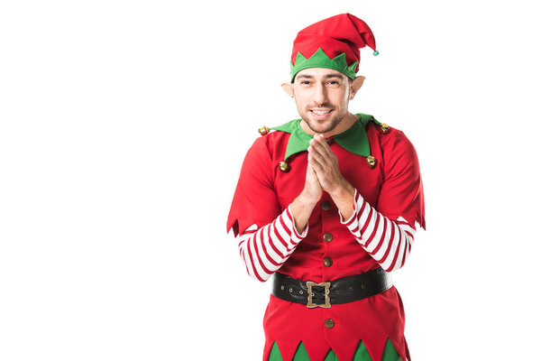 smiling man in christmas elf costume looking at camera and rubbing hands in anticipation isolated on white