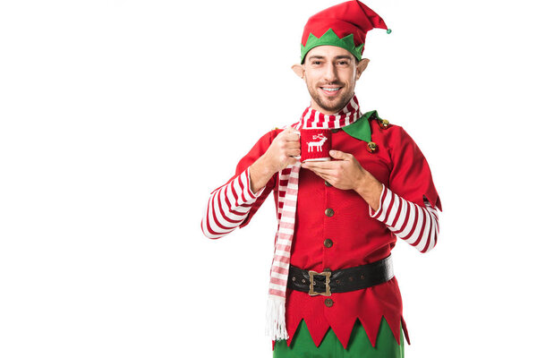 улыбающийся мужчина в рождественском костюме эльфа держит чашку чая и смотрит на камеру, изолированную на белом
