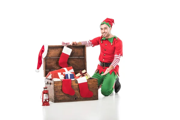 クリスマス ストッキングと白で隔離プレゼント木製のたんすの上に座ってクリスマス エルフ衣装で男  — 無料ストックフォト