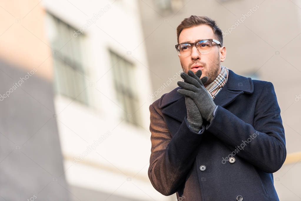 handsome man warming hands with blurred building
